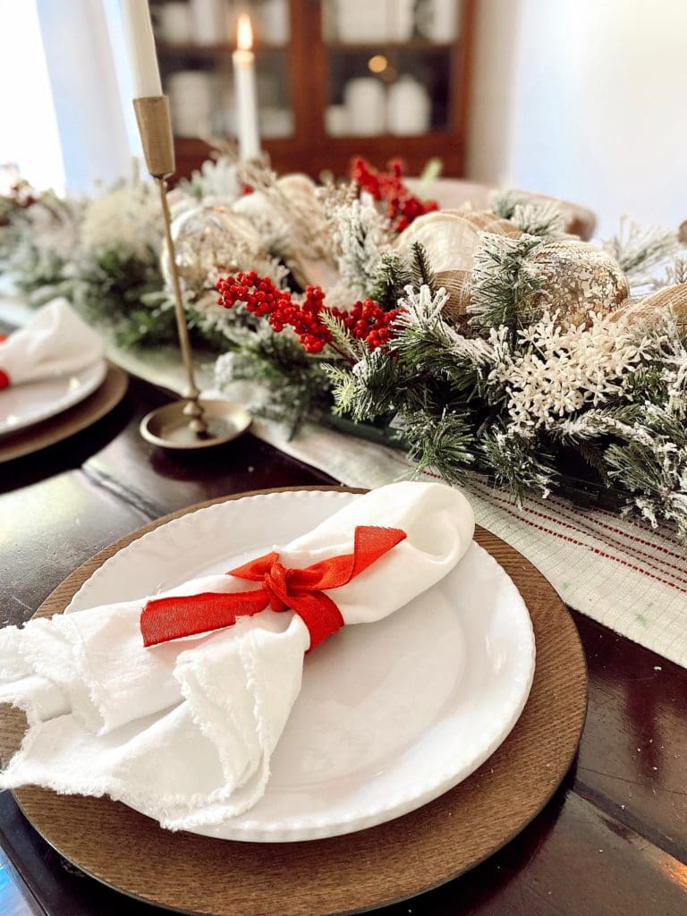 table scape with garland down the middle of the table with white napkins tied with red ribbon at every place setting