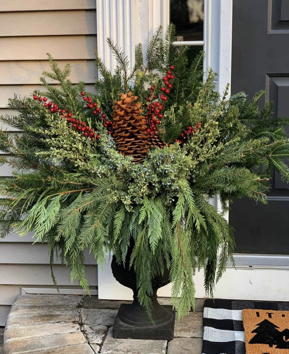 christmas greenery arranged in a winter planter with red berries and a large pine cone