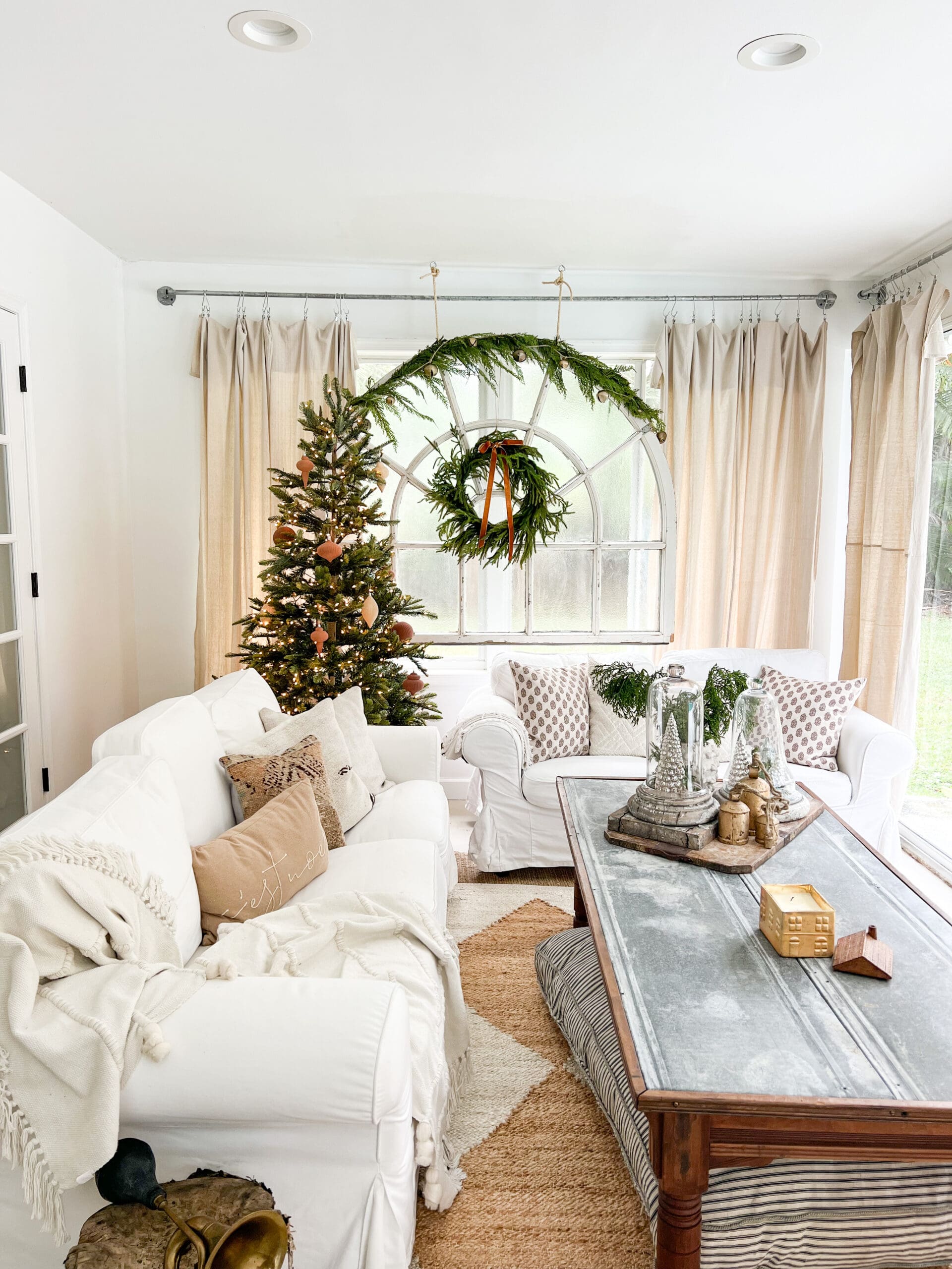 view of living space with a sparse Christmas tree, a large window styled with greenery, and a cozy white couch with comfy Christmas pillows