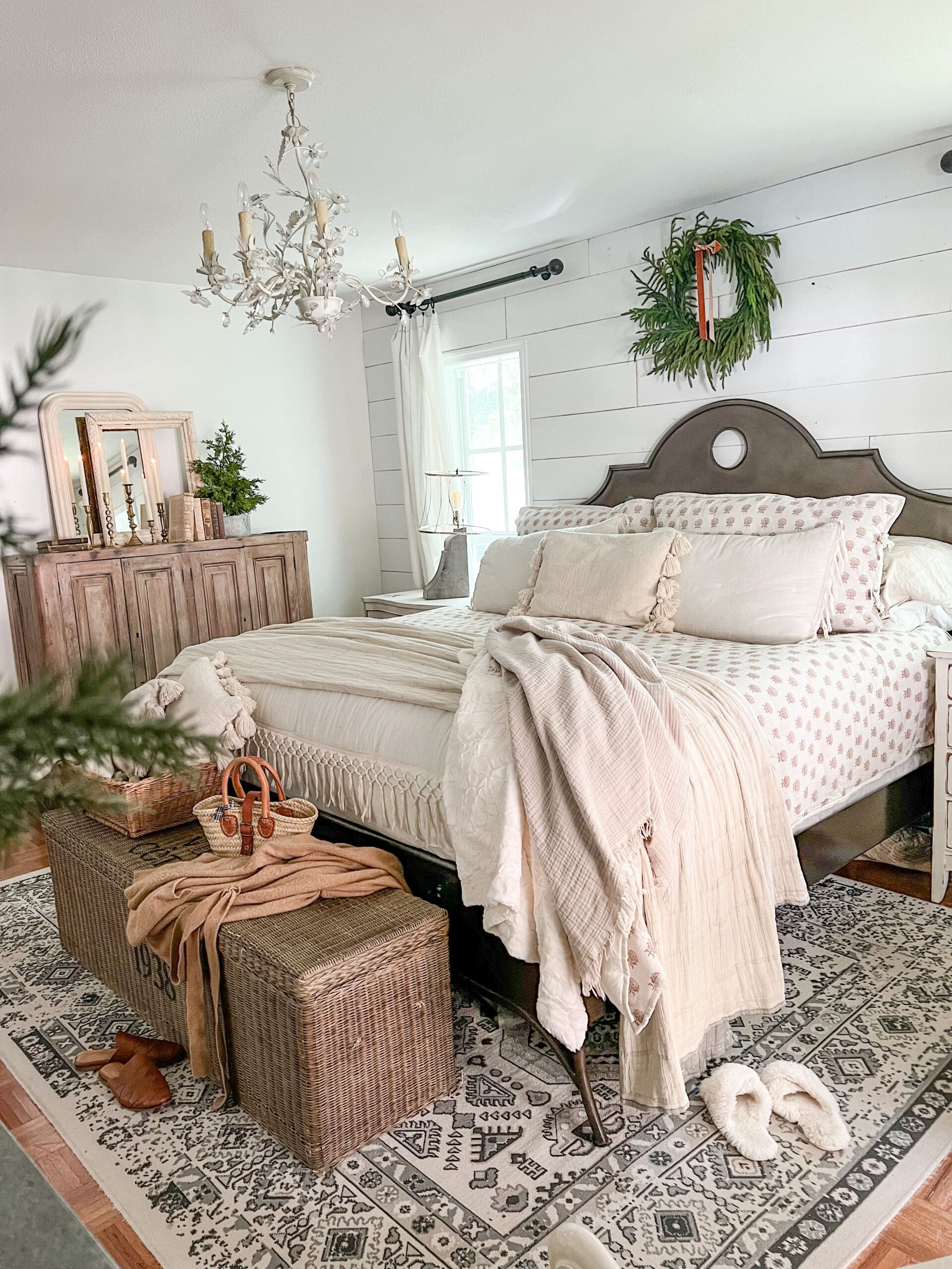 cozy bedroom styled with neutral bedding, a large weaved basket and a throw blanket on top, and a small wreath above the bed