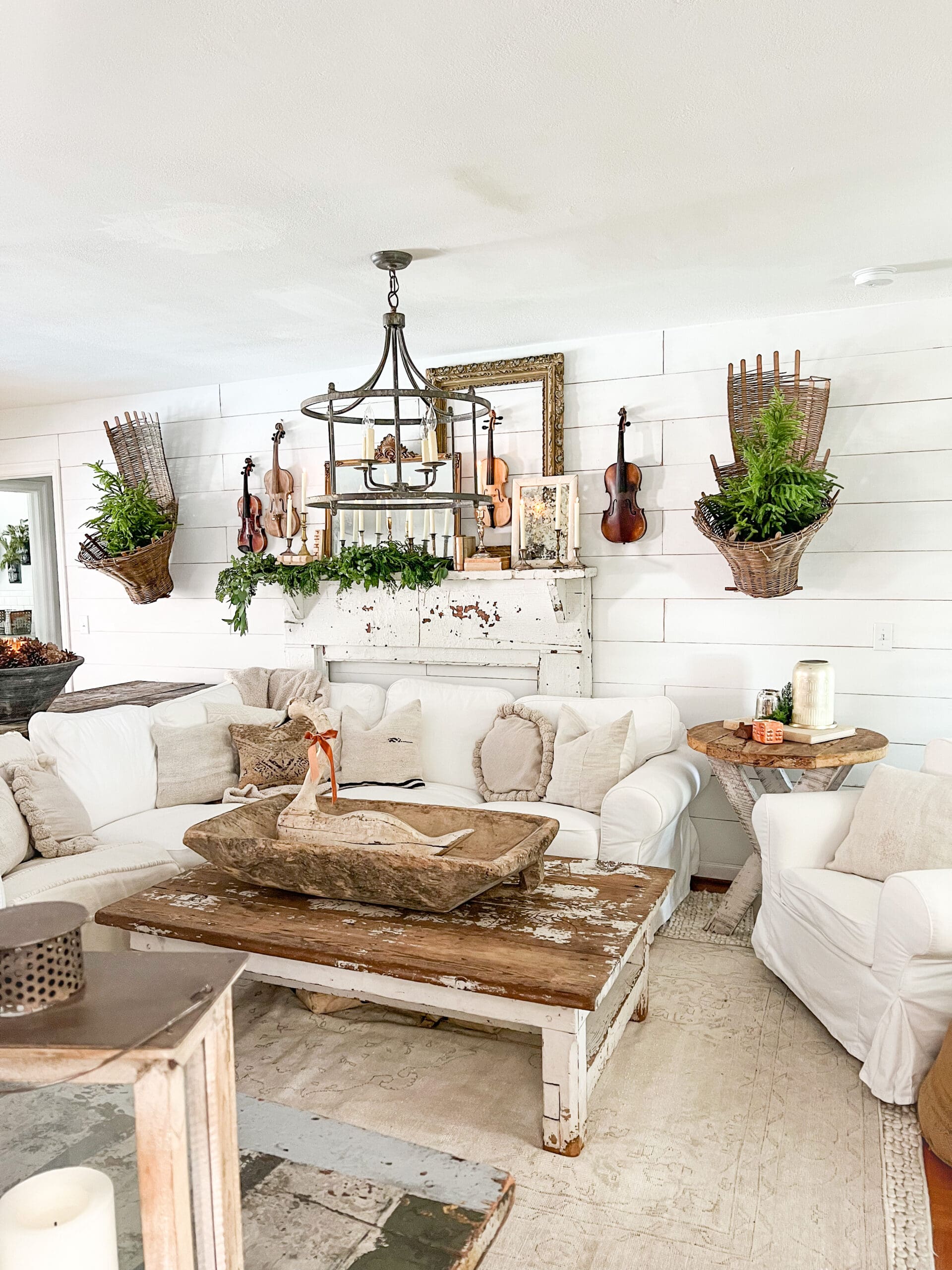 family room styled for winter with small winter trees hanging in baskets on a wall and a gallery wall with winter decor