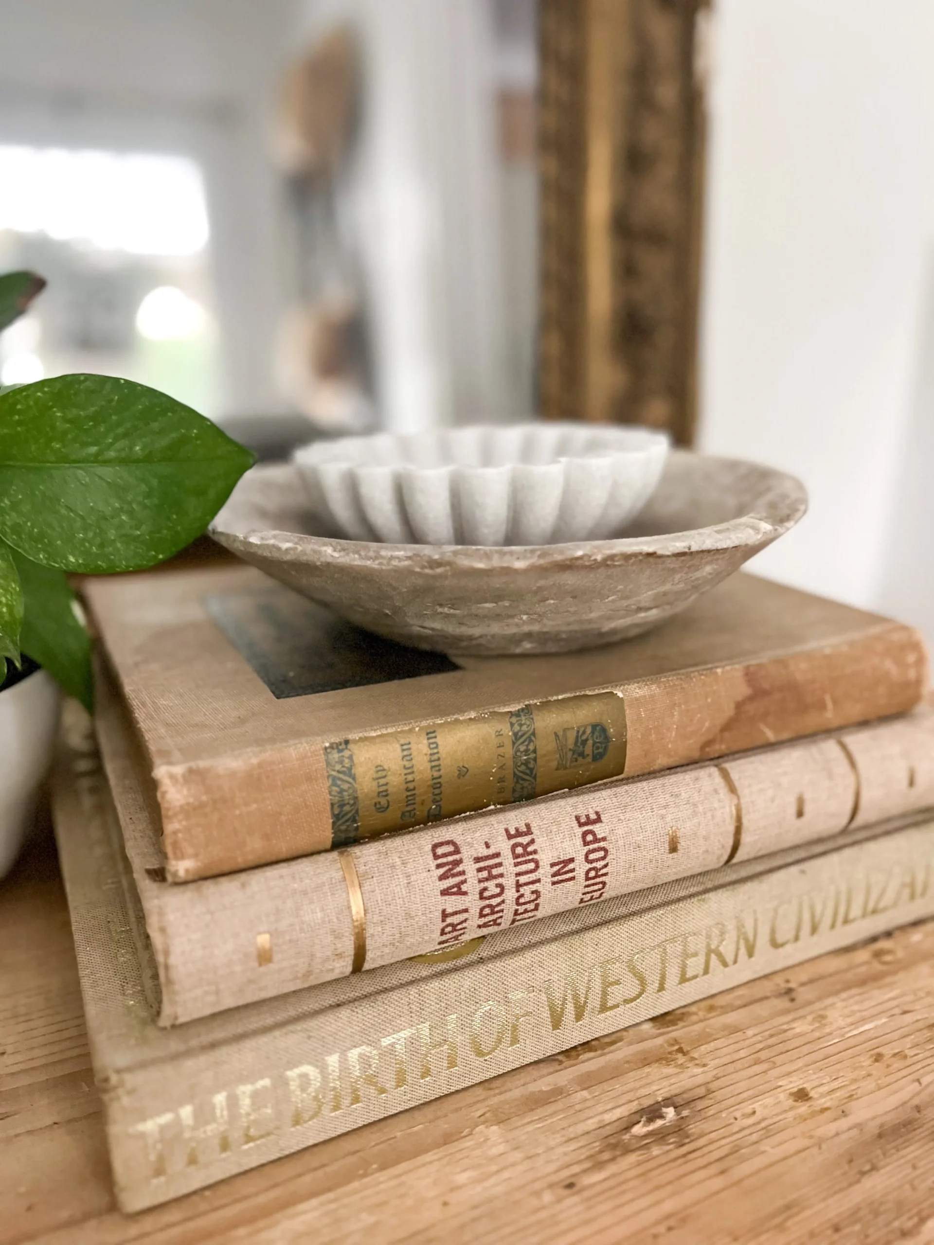 stack of different vintage books with a small ironstone bowl with scalloped edges on top