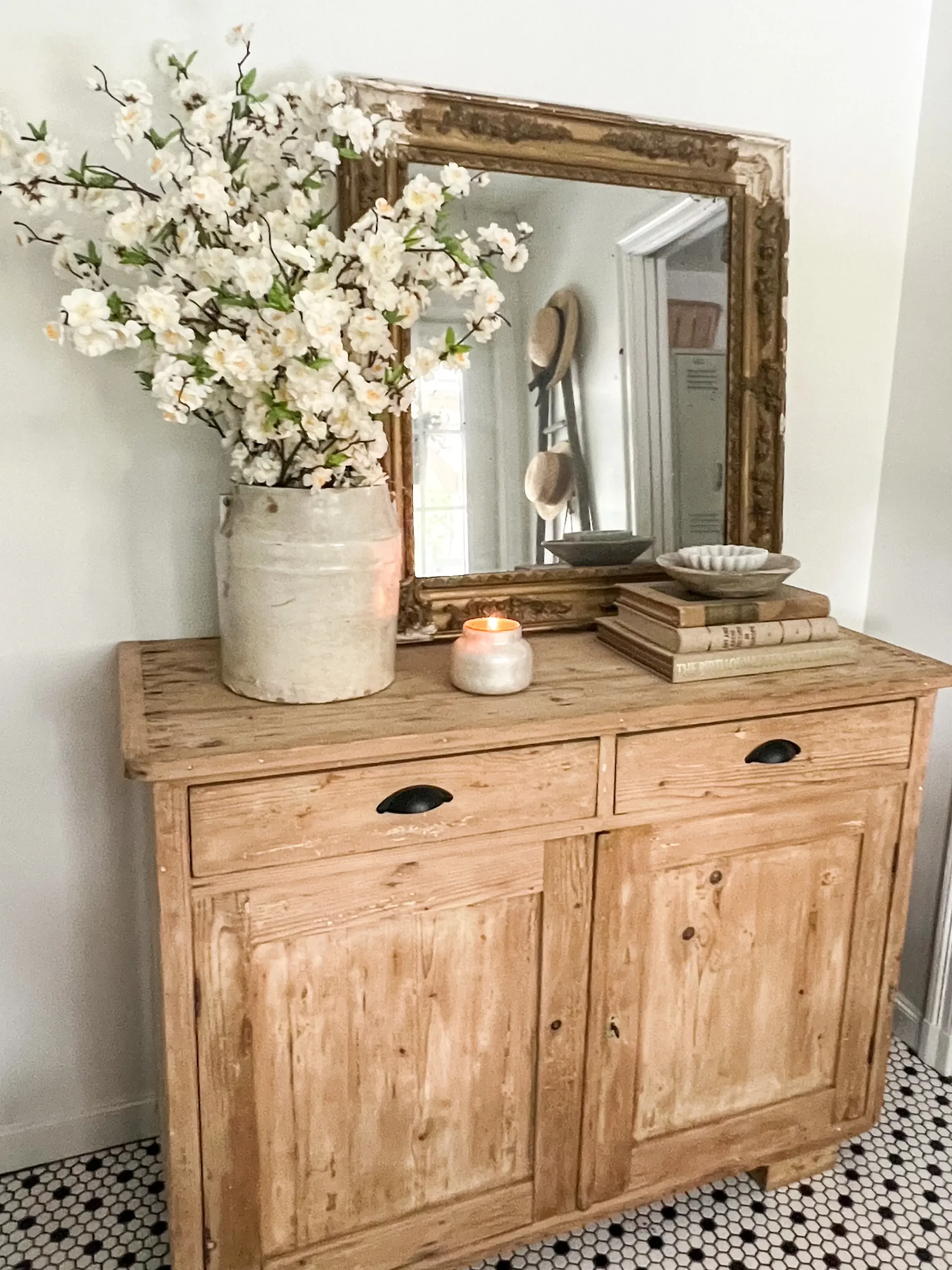 wooden console table styled with cherry blossoms, a large mirror, a small stack of vintage books and a small candle