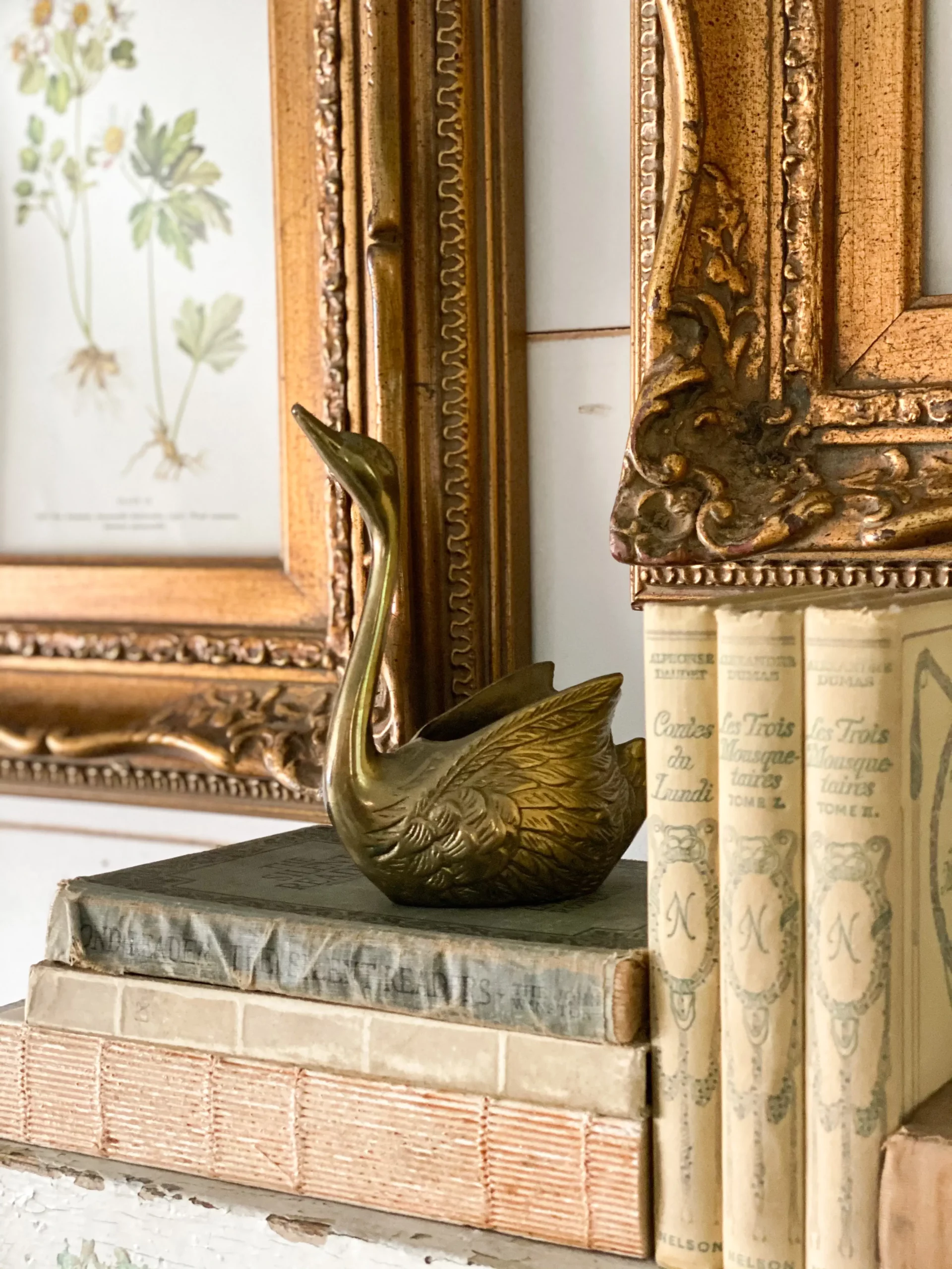beautiful vintage books stacked on a mantel with a small brass goose on top