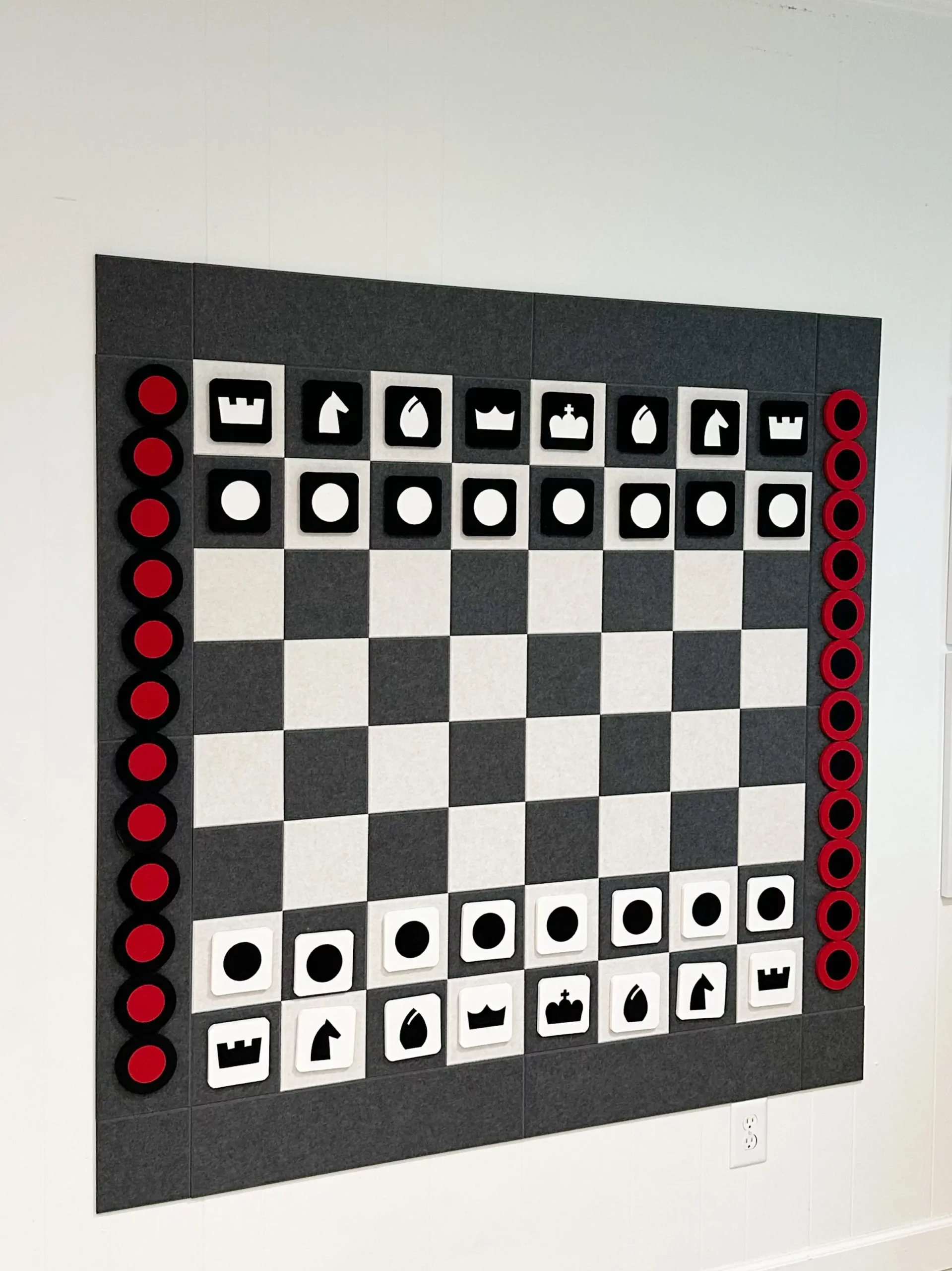 large black and white felt chessboard mounted on a white wall with all the felt pieces for chess and checkers on the sides