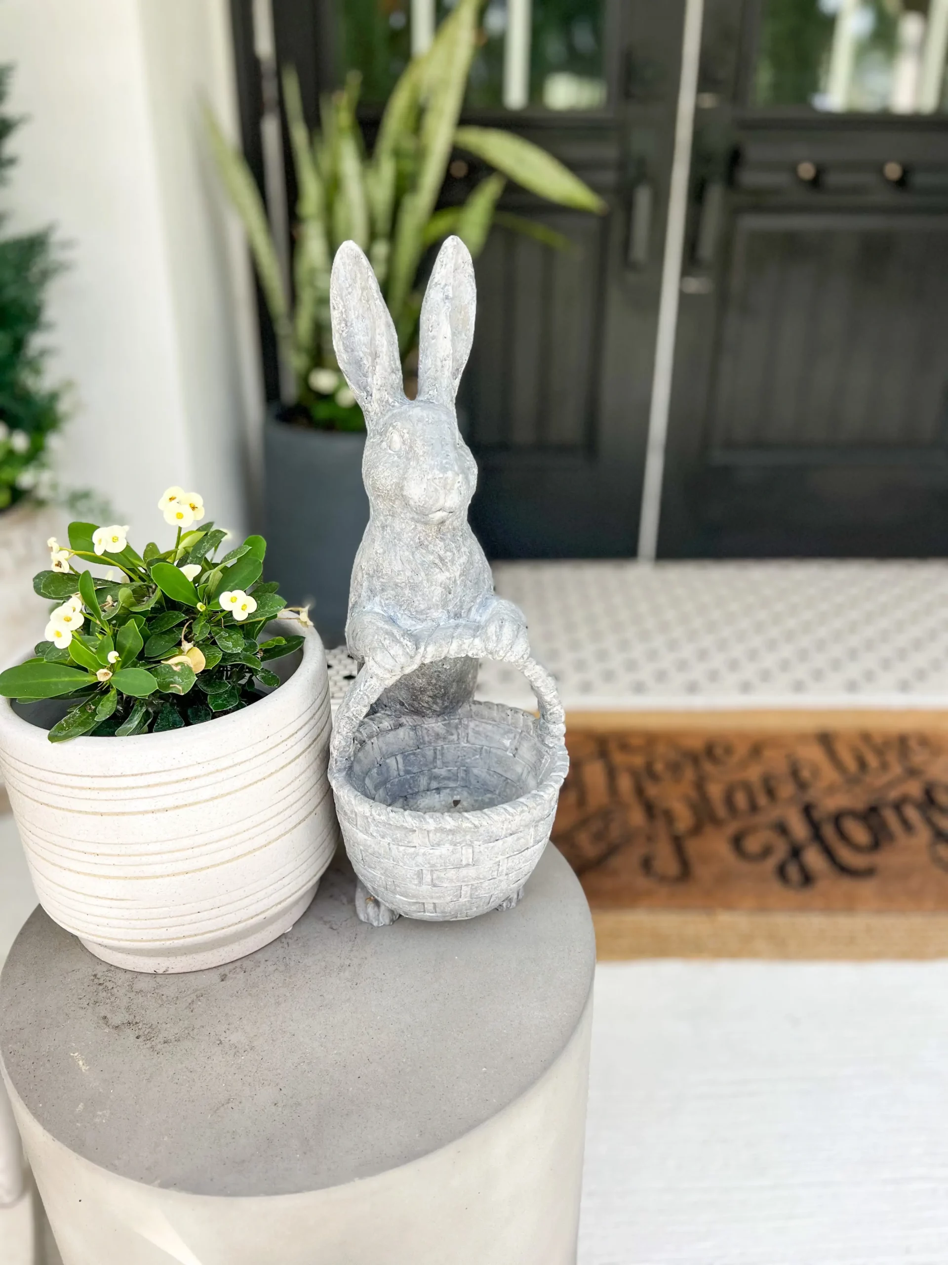 small concrete bunny sitting next to a small plant on a side table on the front porch