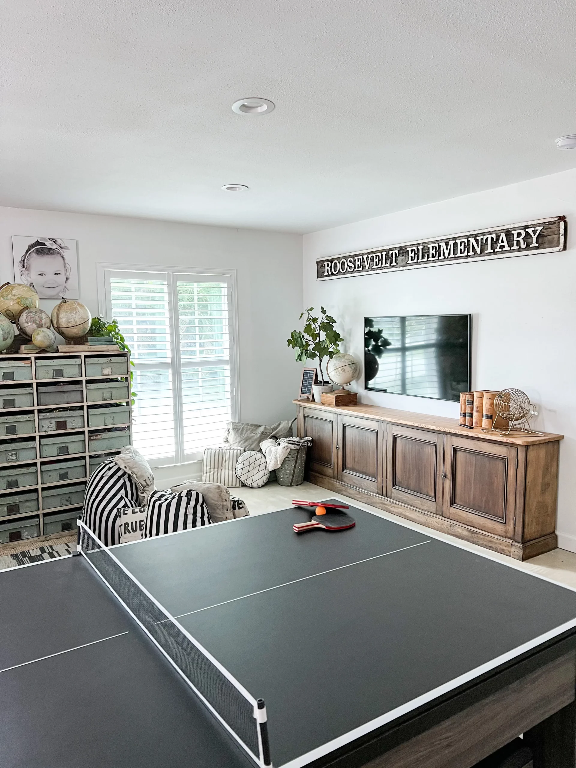 view of a beautiful neutral playroom with a ping pong table, striped bean bags, and a TV