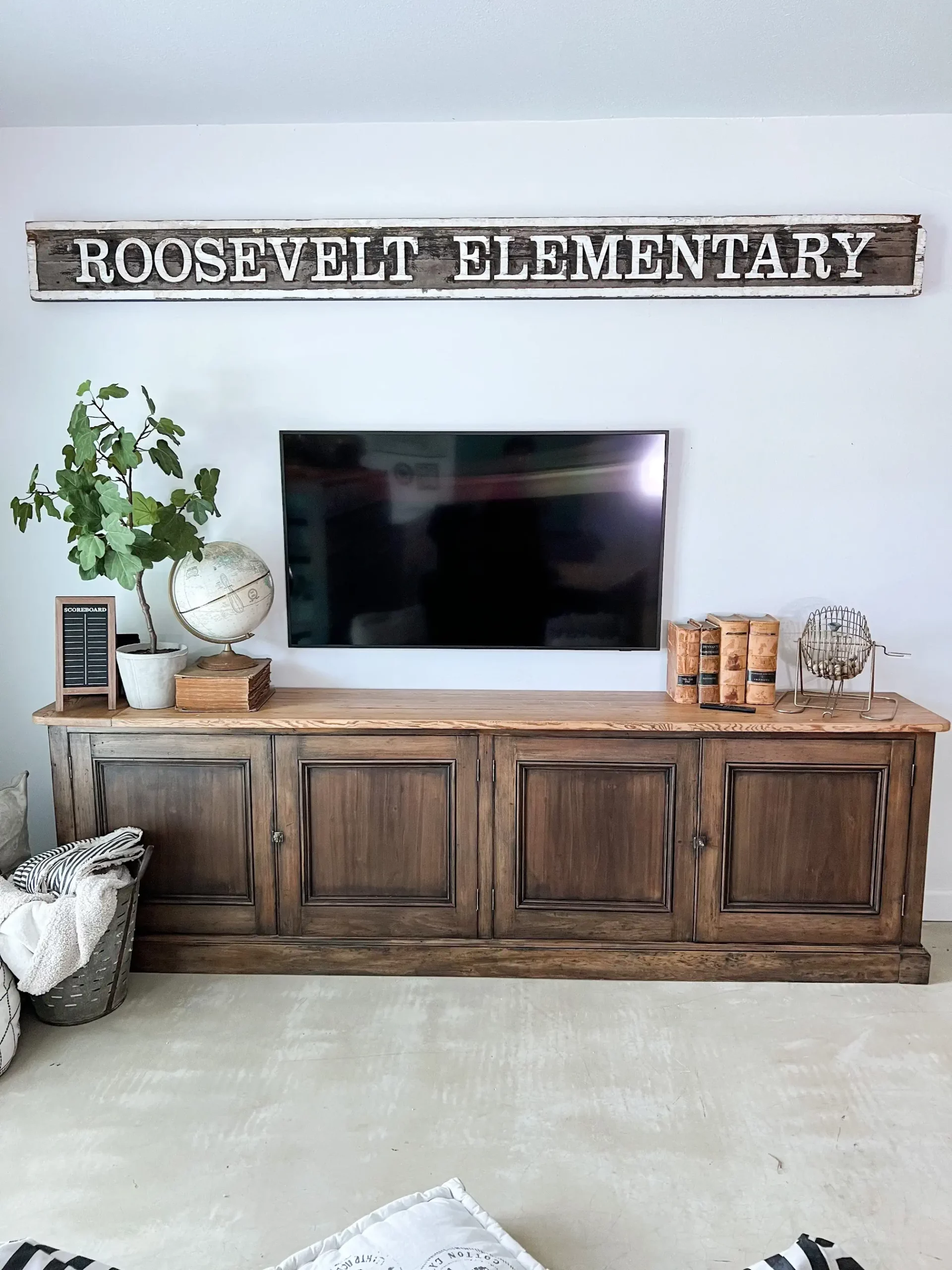 large wooden console table styled with books and a plant with a TV above it as well as a sign that says "Roosevelt Elementary"