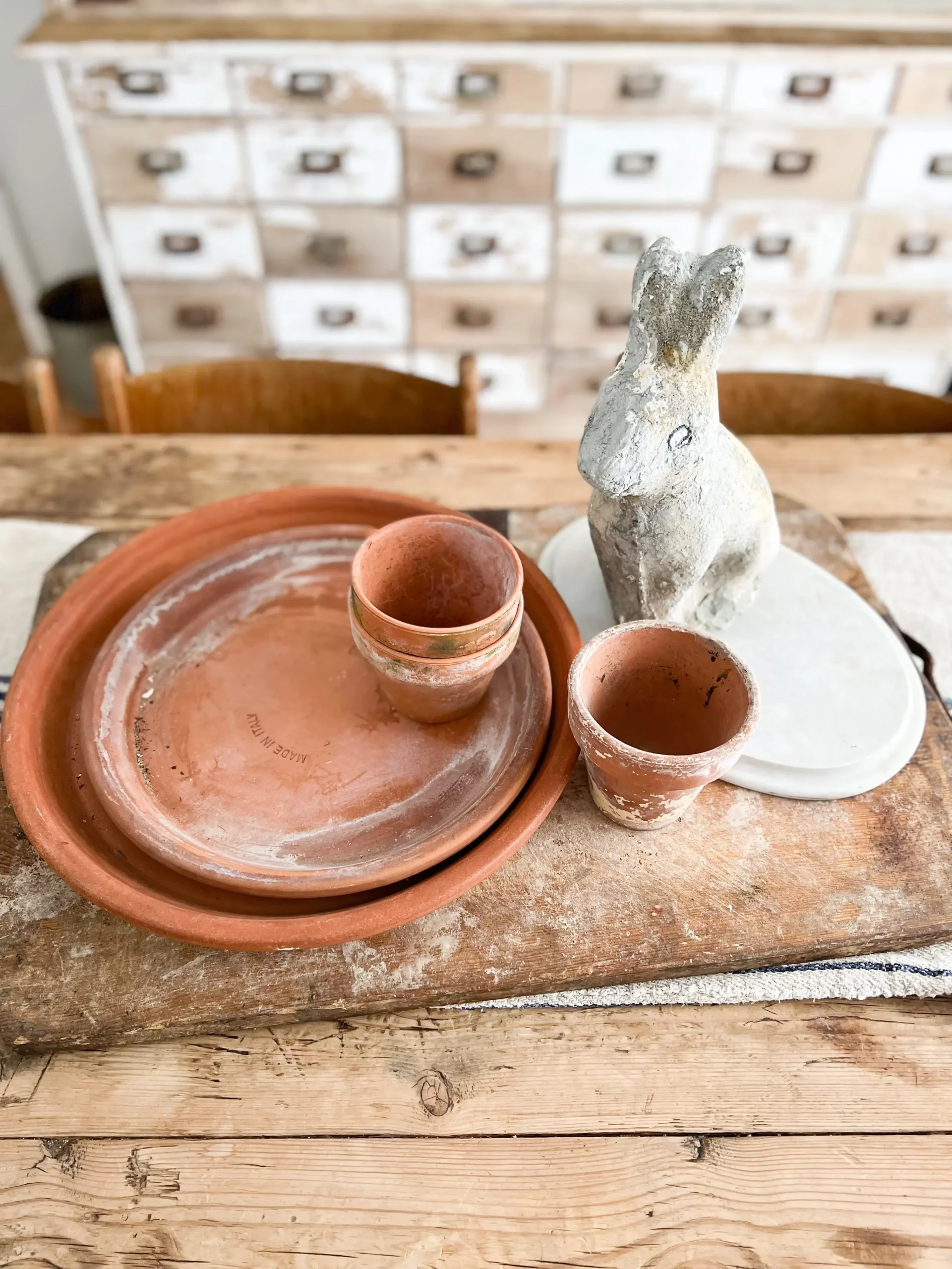 closeup of a bread board with terracotta saucers and pots as well as a cement bunny on top