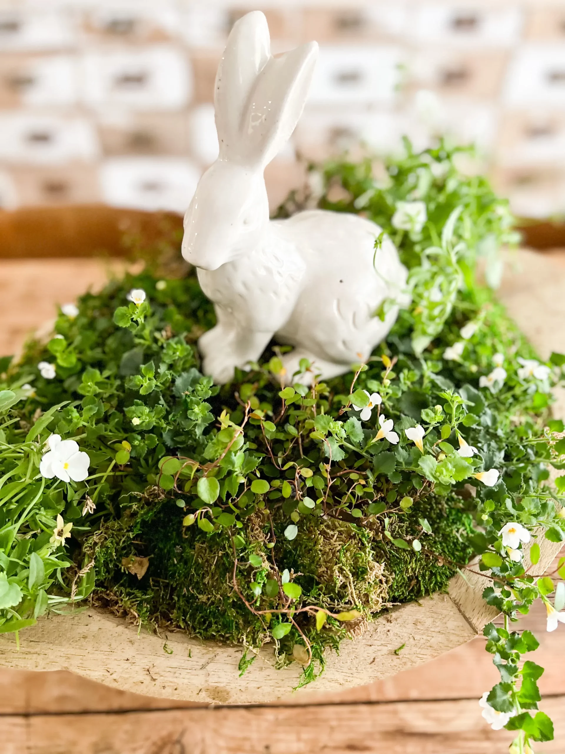 adorable white bunny on top of a wooden bowl with greenery and small white flowers