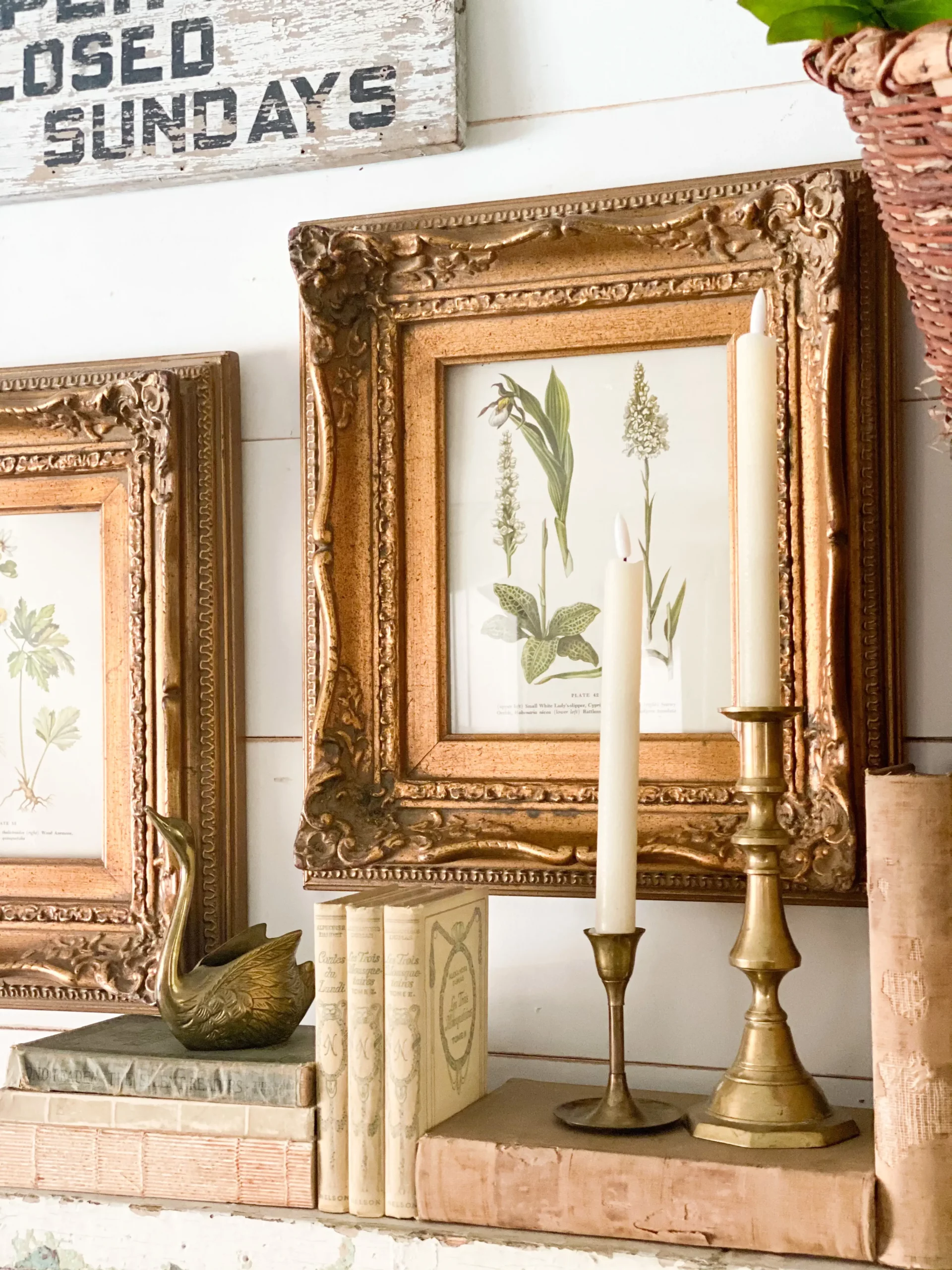 vintage art floral print inside a wide gold frame hanging above a chippy white mantel