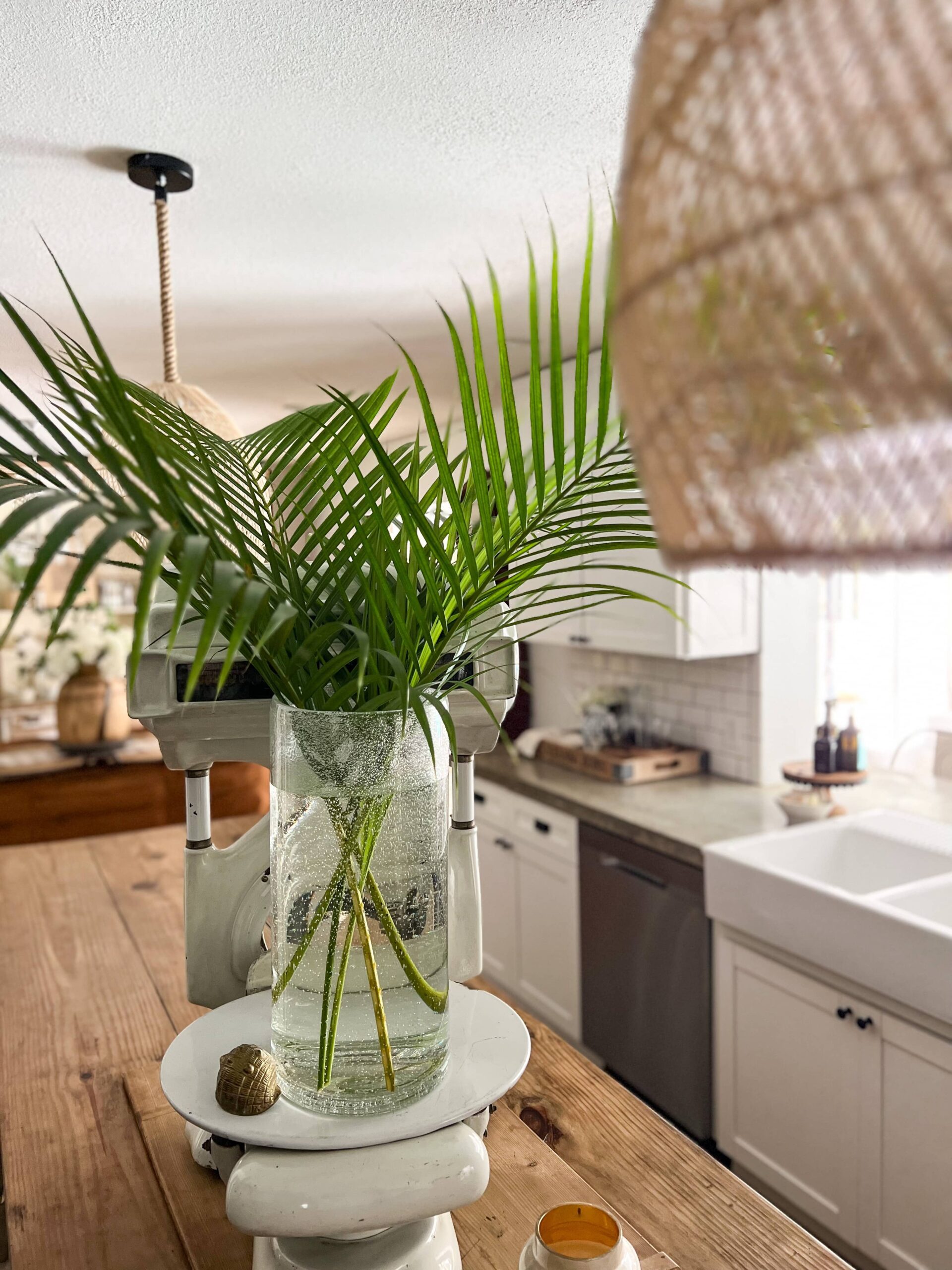 glass vase of palm fronds on top of a white vintage scale in the center of a kitchen island