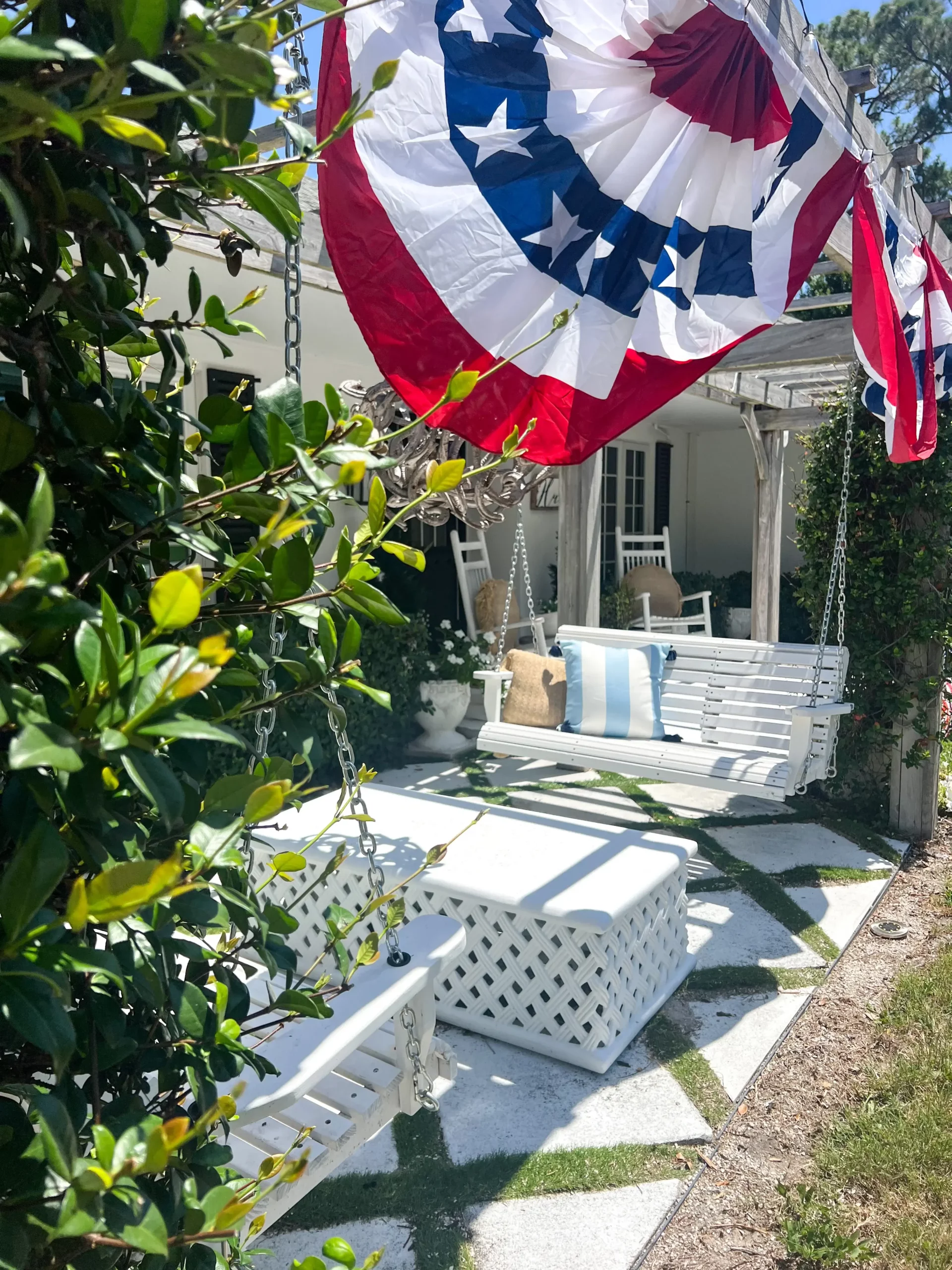 bunting hanging from pergola with summer pillows on the white porch swings