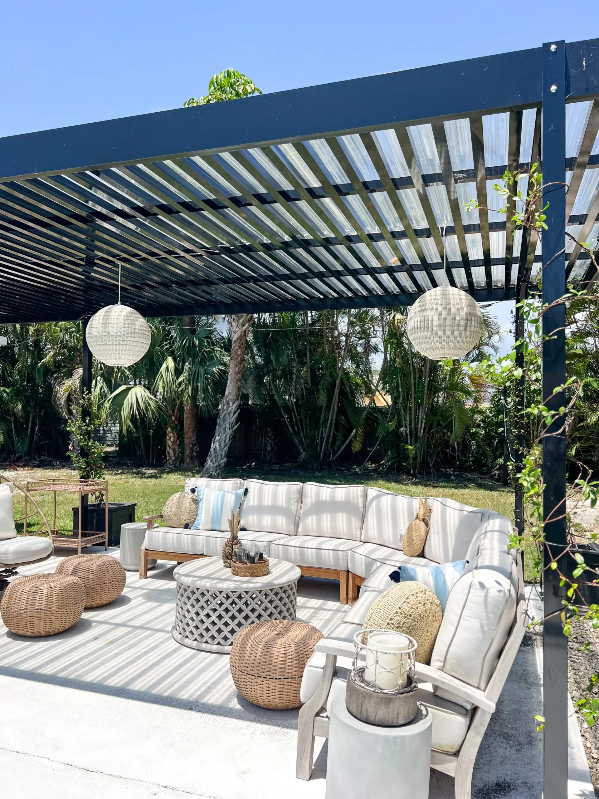 beautiful black pergola with rattan lights hanging from it, a large sectional with summer pillows, and a beautiful outdoor coffee table